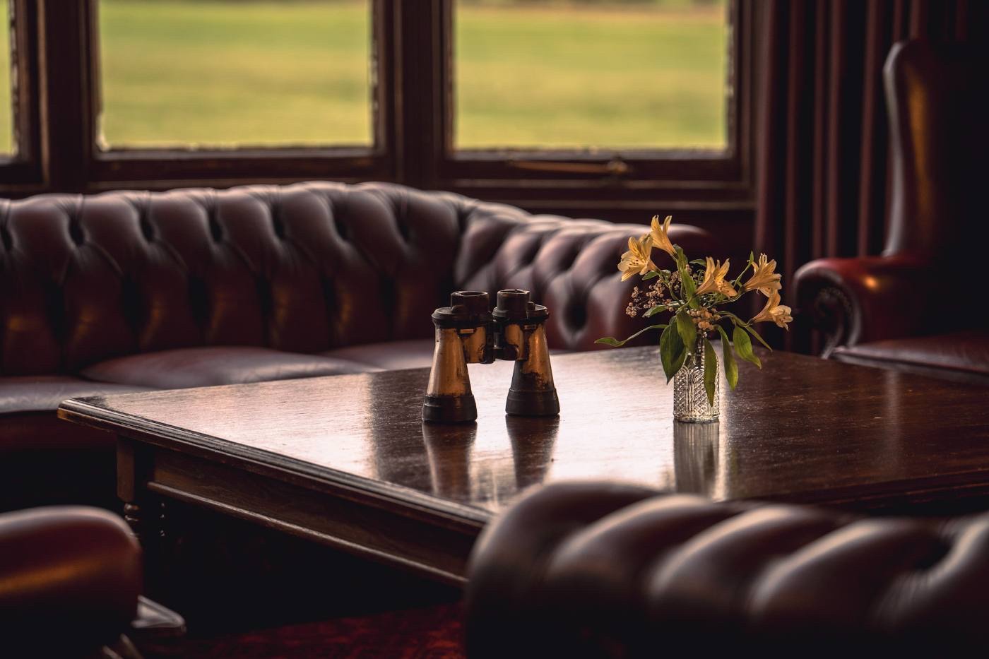 A leather chesterfield banquette with a table set with cruets and a small vase of flowers, windows onto the course