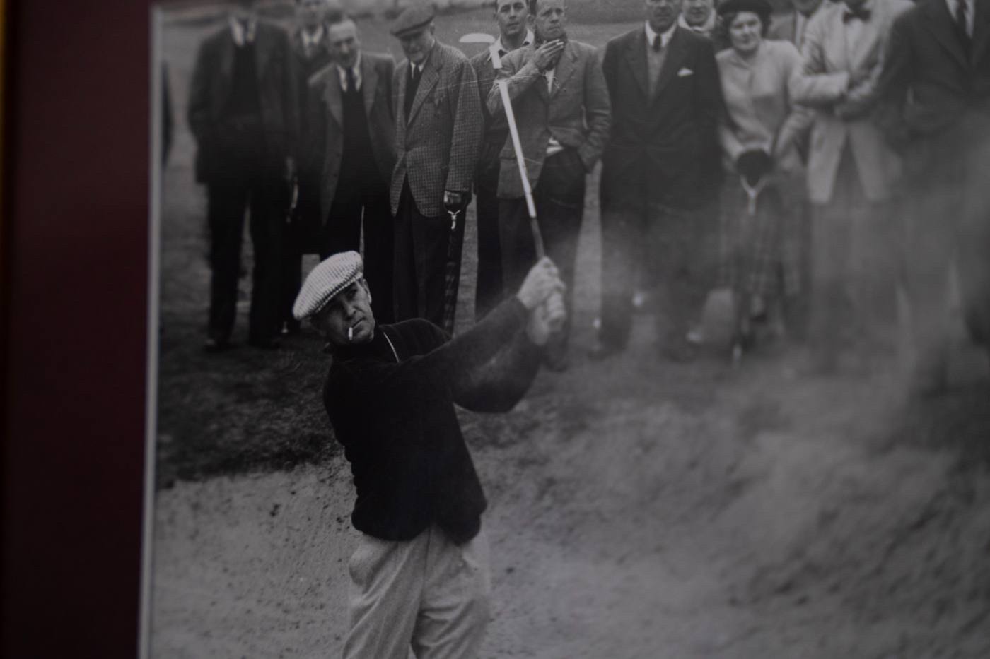 Ben Hogan playing a bunker shot, sand exploding, a crowd of spectators in period dress watching from behind