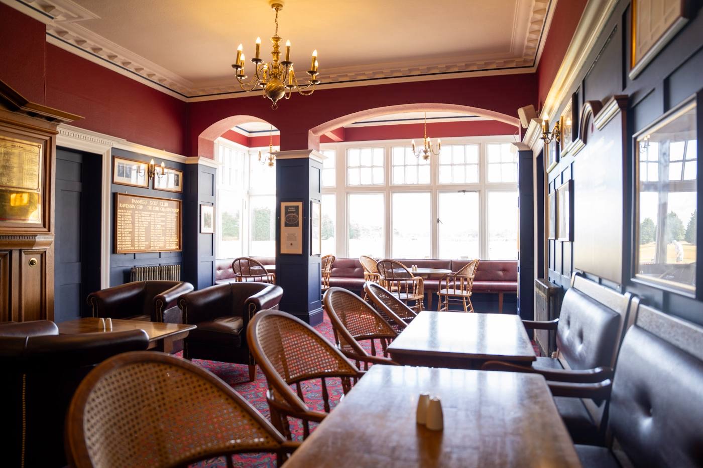 The clubhouse lounge with honours boards, long tables and cane chairs, windows onto the course